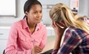 Woman in a pink shirt, holding pen, listening and counselling a teen girl